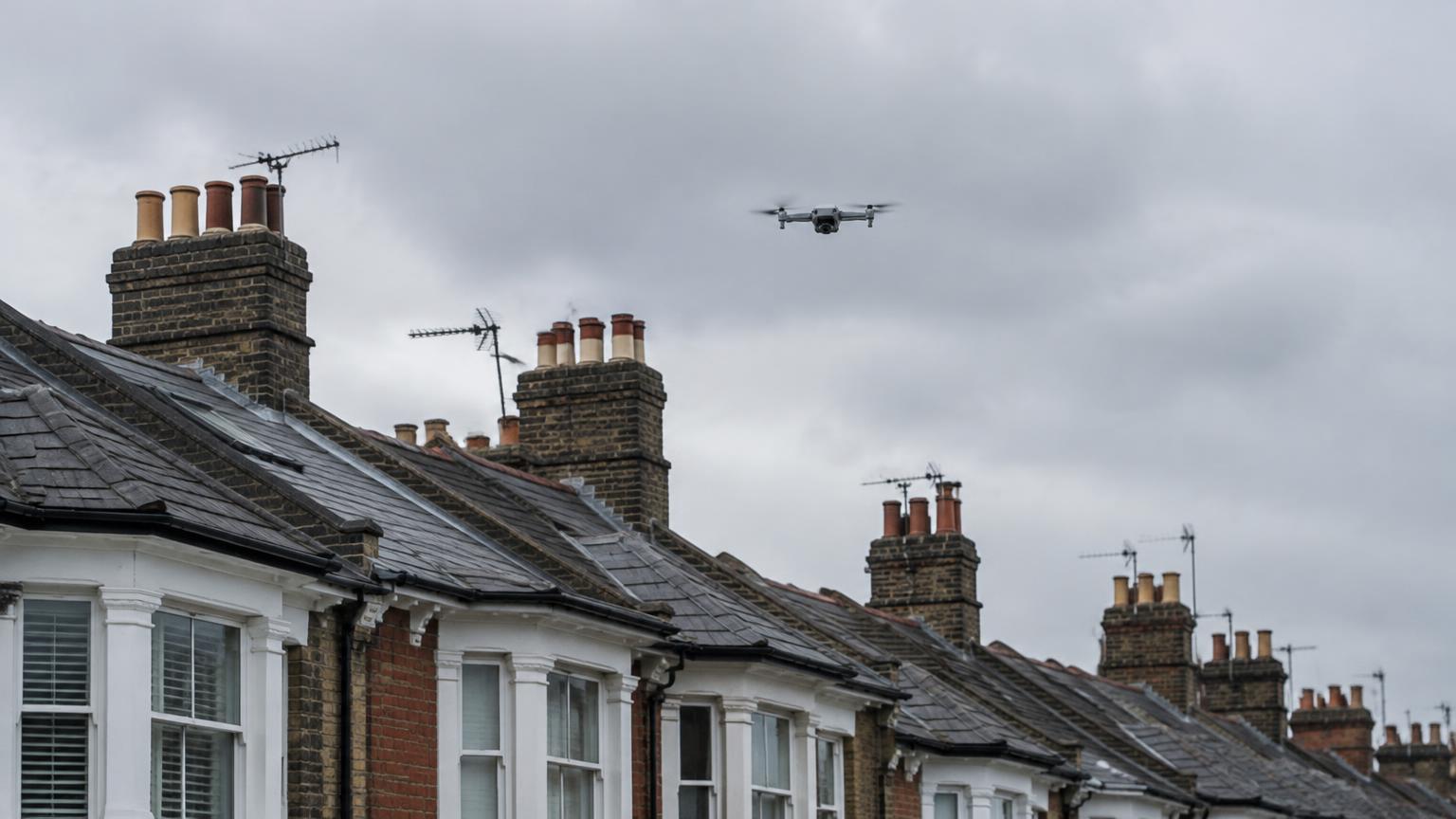 Survey drone flying above a row of London terraced roofs and chimneys